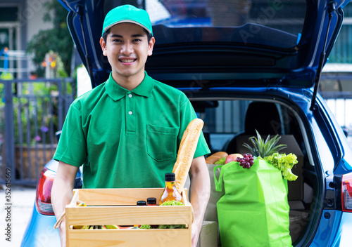 Asian delivery man in green t-shirt delivering food, fruit, joice and vegetable to home - online grocery shopping service concept photo