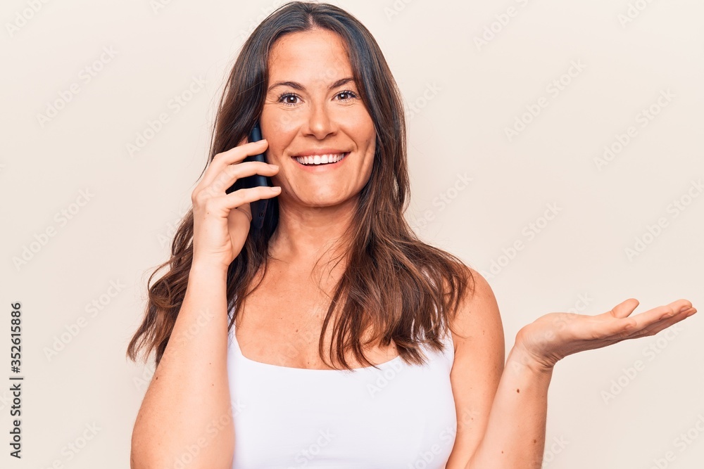 Beautiful brunette woman having conversation talking on the smartphone over white background celebrating achievement with happy smile and winner expression with raised hand Beautiful brunette woman having conversation talking on the smartphone over white background celebrating achievement with happy smile and winner expression with raised hand