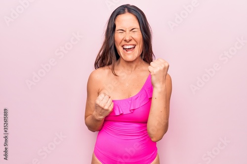 Young beautiful brunette woman wearing pink swimwear standing over isolated background celebrating surprised and amazed for success with arms raised and eyes closed