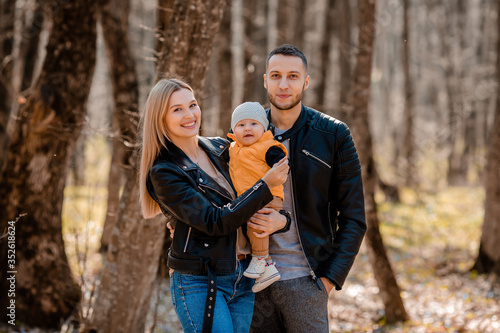 young family walk in the park in the spring with a toddler in a stroller. Happy parents