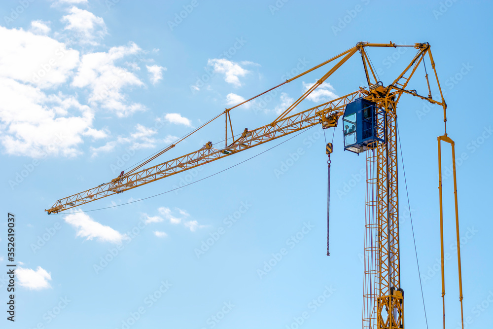 Industrial construction building crane. Yellow mobile rotary crane with a cabin of the operator against a blue sky. Large tall machine used for moving heavy objects. Industrial construction building crane. Yellow mobile rotary crane with a cabin of the operator against a blue sky. Large tall machine used for moving heavy objects.