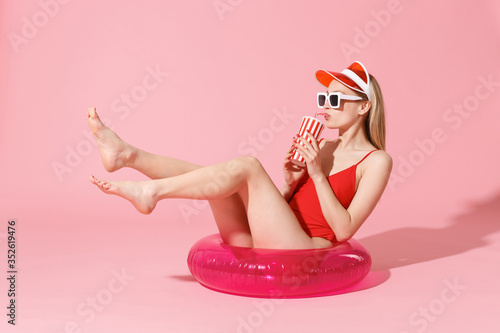 Cuadro en lienzo Beautiful young blonde woman in red one-piece swimsuit cap sunglasses isolated on pink background