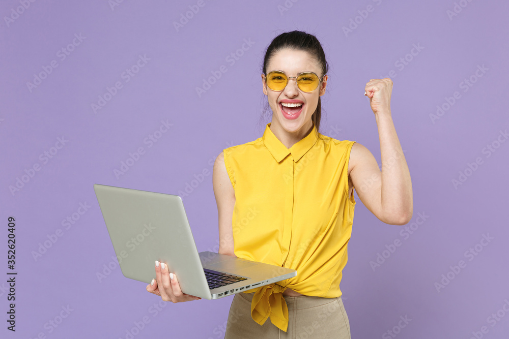 Joyful young brunette woman girl in yellow casual shirt posing isolated on violet background studio. People lifestyle concept. Mock up copy space. Working on laptop pc computer, doing winner gesture. Joyful young brunette woman girl in yellow casual shirt posing isolated on violet background studio. People lifestyle concept. Mock up copy space. Working on laptop pc computer, doing winner gesture.