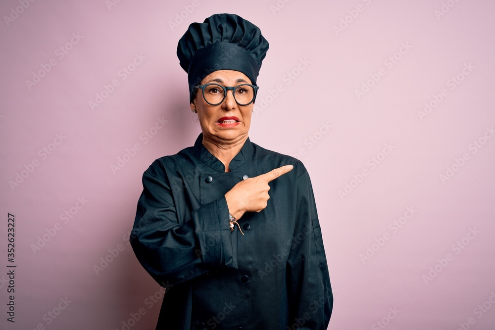 Middle age brunette chef woman wearing cooker uniform and hat over isolated pink background Pointing aside worried and nervous with forefinger, concerned and surprised expression Middle age brunette chef woman wearing cooker uniform and hat over isolated pink background Pointing aside worried and nervous with forefinger, concerned and surprised expression