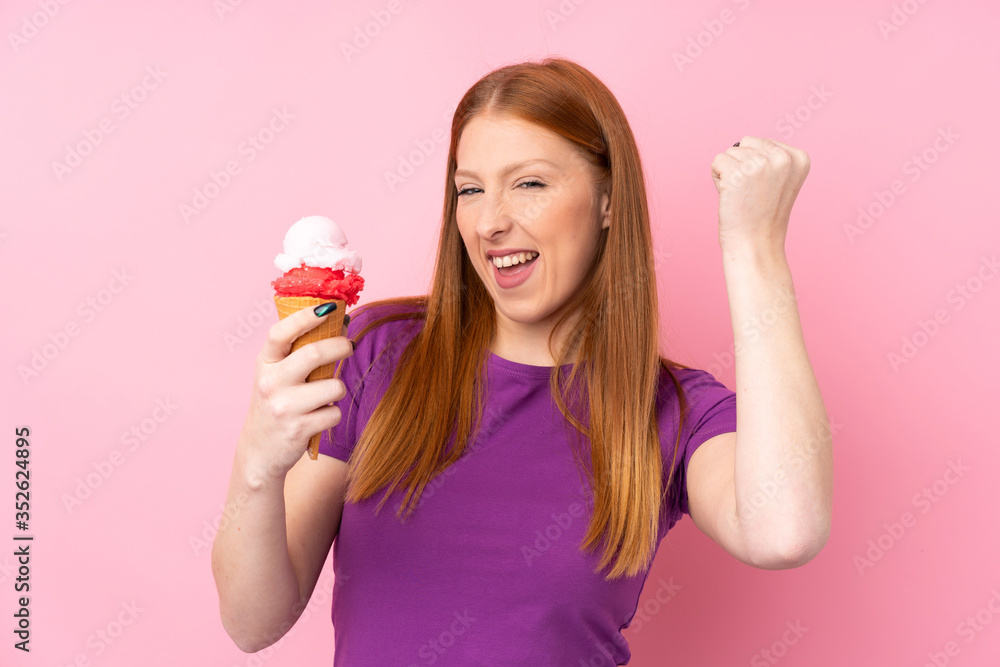 Young redhead woman with a cornet ice cream over isolated pink background celebrating a victory Young redhead woman with a cornet ice cream over isolated pink background celebrating a victory