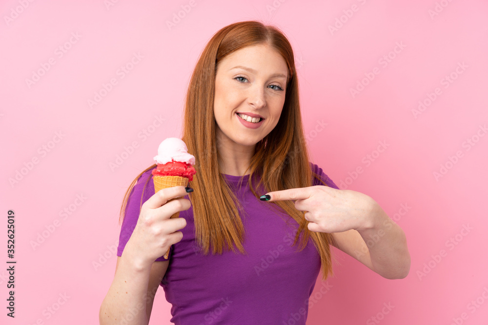 Young redhead woman with a cornet ice cream over isolated pink background and pointing it Young redhead woman with a cornet ice cream over isolated pink background and pointing it