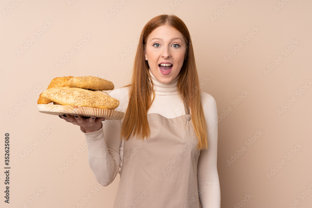 Young redhead woman in chef uniform. Female baker holding a table with several breads with surprise and shocked facial expression Young redhead woman in chef uniform. Female baker holding a table with several breads with surprise and shocked facial expression