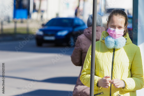 Girl in a medical mask stands near the road.
