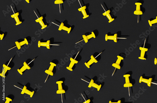 A pattern of scattered yellow office pushpins on a black background. Hard light, shadows.