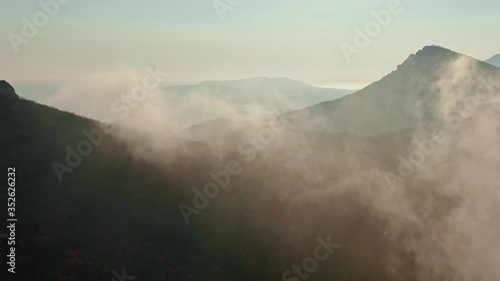 aerial survey flying over the slopes of the mountains overgrown forest and covered with fog in the autumn sunset