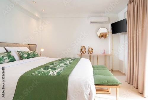 Modern ecological style interior of hotel room with empty wall copy space. Side view of white bedroom with green palm leaves bedding