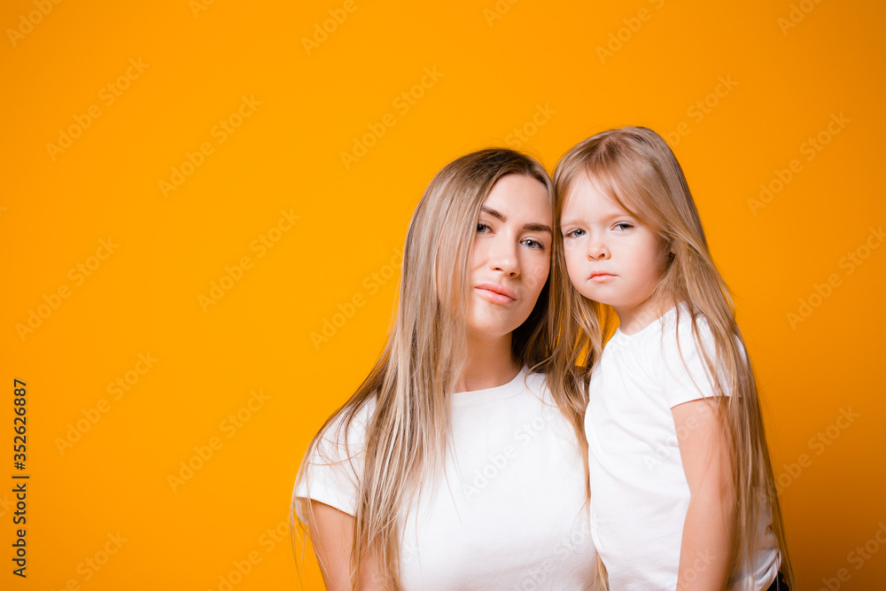 Mom and daughter are not happy that they are sitting on self-isolation. Portrait of a family on an orange background Mom and daughter are not happy that they are sitting on self-isolation. Portrait of a family on an orange background