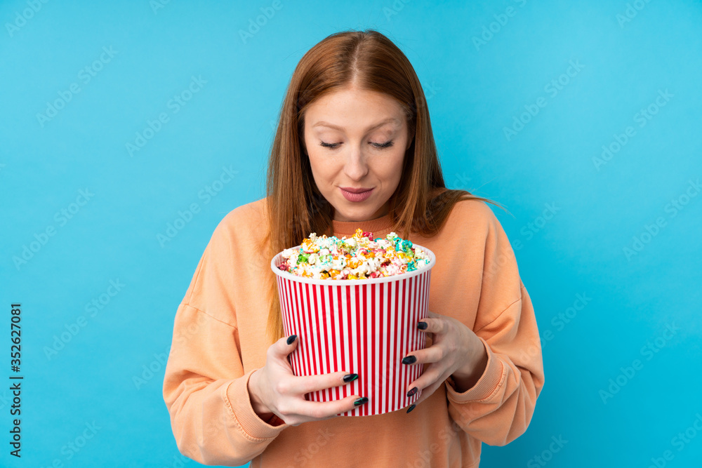 Young redhead woman over isolated background holding a big bucket of popcorns