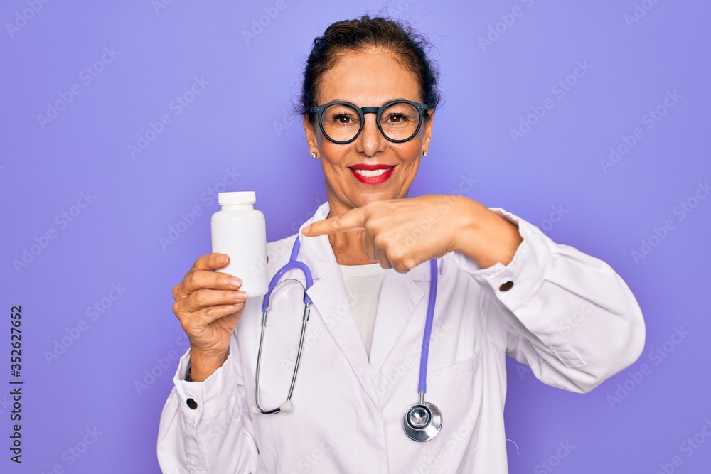 Middle age senior professional doctor woman holding pharmaceutical pills very happy pointing with hand and finger Middle age senior professional doctor woman holding pharmaceutical pills very happy pointing with hand and finger