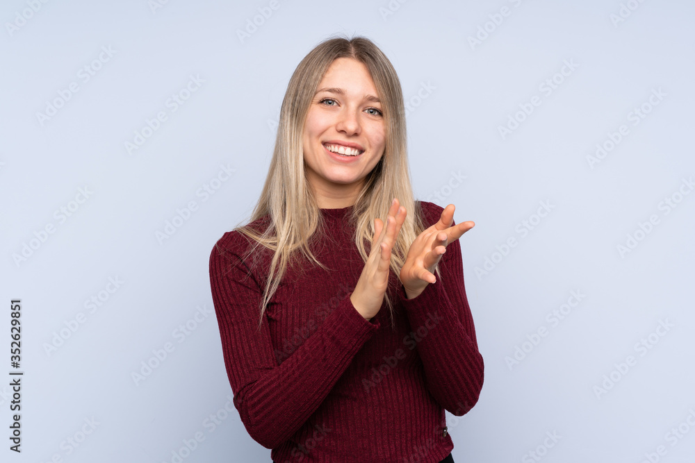 Young blonde woman over isolated blue background applauding after presentation in a conference Young blonde woman over isolated blue background applauding after presentation in a conference