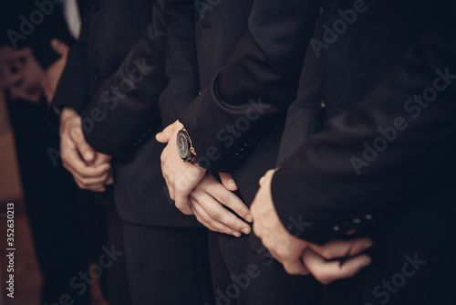 Men in black suits his hands clasped