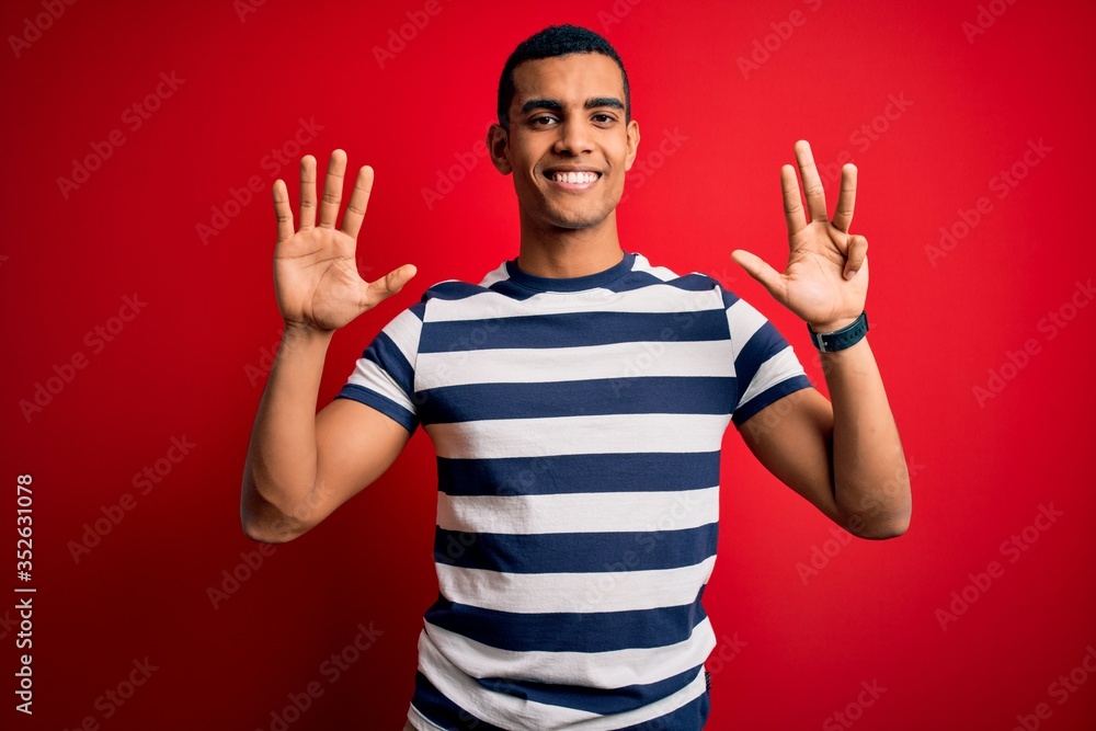 Handsome african american man wearing casual striped t-shirt standing over red background showing and pointing up with fingers number nine while smiling confident and happy. Handsome african american man wearing casual striped t-shirt standing over red background showing and pointing up with fingers number nine while smiling confident and happy.