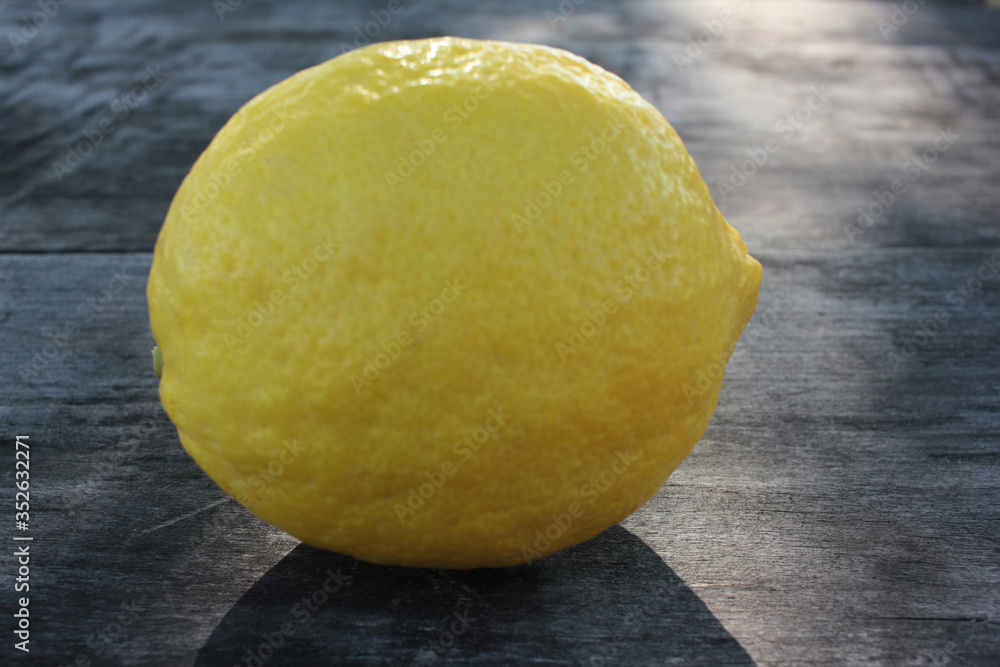 Whole single lemon fruit on rough wooden background in sunny day

