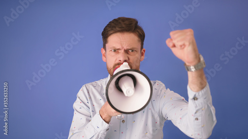 Angry man shouting into the loudspeaker. Isolated on blue background. Copy space.