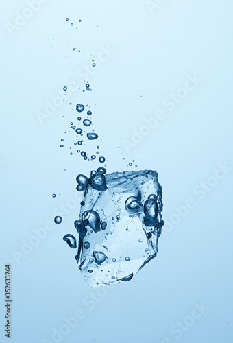 Ice piece falling in the water with bubbles. Cold water, ice cube, ice chunk. Light blue background. High speed photography  