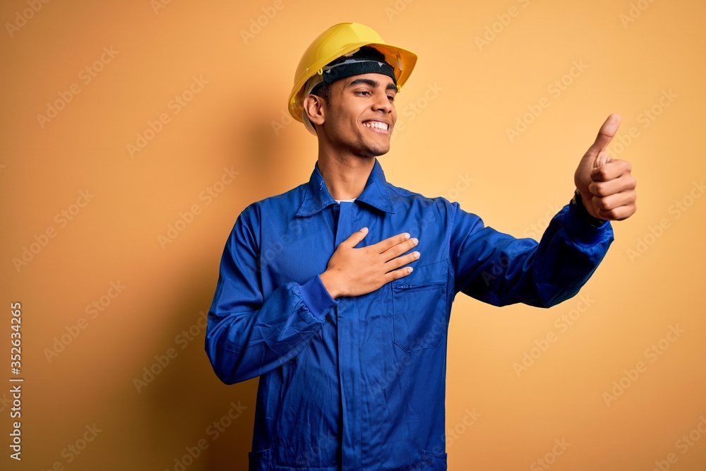 Young handsome african american worker man wearing blue uniform and security helmet Looking proud, smiling doing thumbs up gesture to the side
