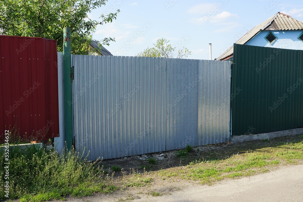 gray closed metal gate and red green fence on a rural street