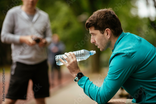 Fit young men taking rest from running. Two friends training outdoors.