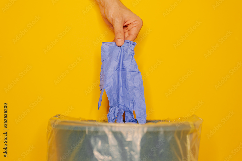 Hand putting used dirty surgical glove to a garbage bin Hand putting used dirty surgical glove to a garbage bin