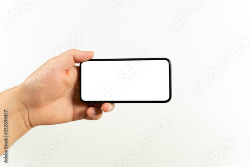 Man hand holding the black smartphone with blank screen and modern frameless design positions horizontal - isolated on white background