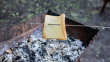 The hand holds a skewer with a piece of bread over the grill. Roasting bread on a campfire