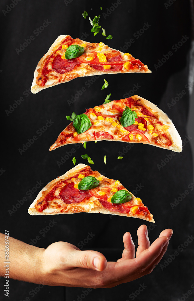 People Hand Taking Three Slices of pizza . Pizza and food concept. Close up focus on middle pizza. Outdoor party background theme. Levitating pizza and vegetables on black background. Vertical photo.