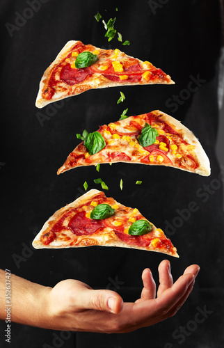 Obraz na płótnie People Hand Taking Three Slices of pizza . Pizza and food concept. Close up focus on middle pizza. Outdoor party background theme. Levitating pizza and vegetables on black background. Vertical photo. w salonie