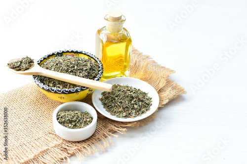 Dried chopped leaves of basil leaves and olive oil on white wooden background