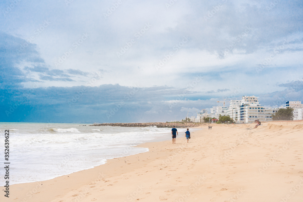 Back view of people walking on a beautiful deserted beach natural seascape cloudy sky landscape outdoors background.