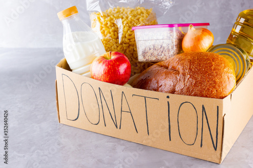 Donation box with food. Open cardboard box with oil, milk, canned food, pasta and bread. Grocery set on gray background. Donation concept