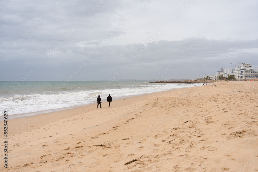 Back view of people walking on a beautiful deserted beach natural seascape cloudy sky landscape outdoors background. Back view of people walking on a beautiful deserted beach natural seascape cloudy sky landscape outdoors background.