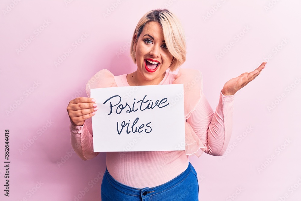 Blonde plus size woman asking for optimist attitude holding paper with positive vibes message celebrating achievement with happy smile and winner expression with raised hand Blonde plus size woman asking for optimist attitude holding paper with positive vibes message celebrating achievement with happy smile and winner expression with raised hand