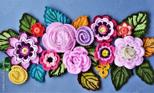 Handmade multicolored crochet flowers and leaves in a row on a grey background.