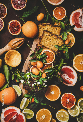 Citrus Mediterranean loaf cake. Flat-lay of almond pound cake with oranges, lemons, kumquats, grapefruits and blossom flowers over dark rusty background, top view. Flourless, vegan dessert concept
