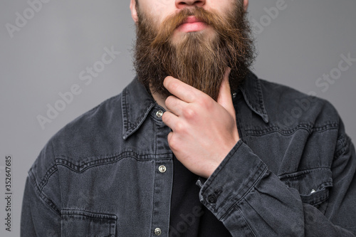 Touching his perfect beard. Close-up of young bearded man touching his beard while standing against grey background photo