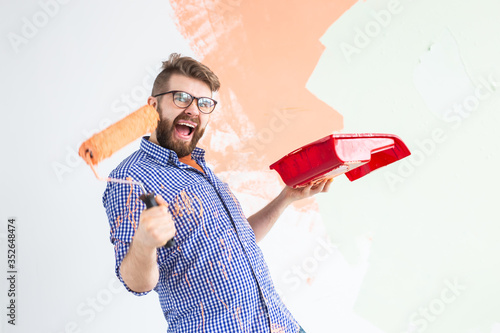 Funny man painting interior wall of home with paint roller. Redecoration, renovation, apartment repair and refreshment concept.