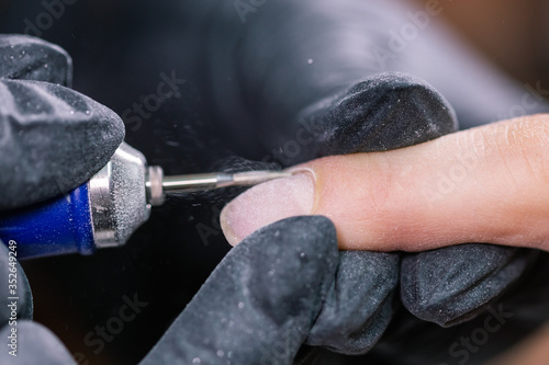 Close-up shot of hardware manicure in a beauty salon. Manicurist is applying electric nail file drill to manicure on female fingers.