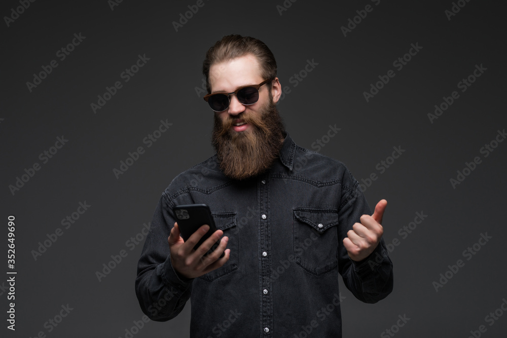 Excited cheerful man wearing shirt using mobile phone celebrating isolated over gray background Excited cheerful man wearing shirt using mobile phone celebrating isolated over gray background