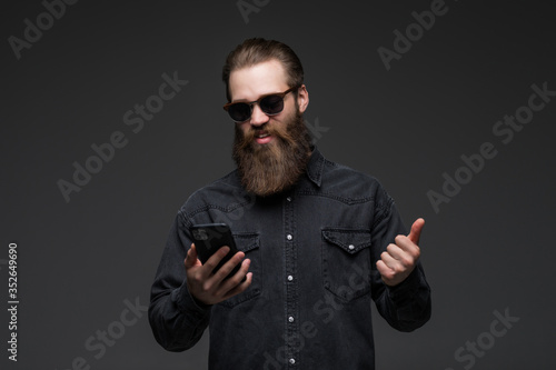 Excited cheerful man wearing shirt using mobile phone celebrating isolated over gray background