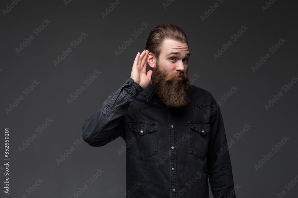 Young man listening something with long beard holding over gray background