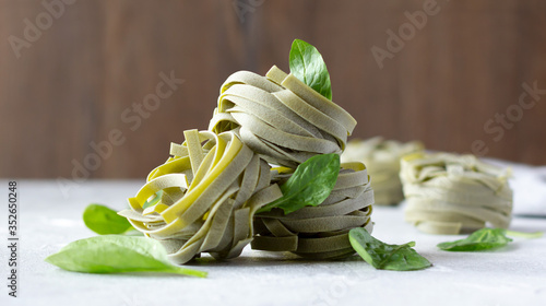 Uncooked spinach pasta tagliatelle (agli spinaci) with fresh spinach leaves, healthy whole wheat pasta nests