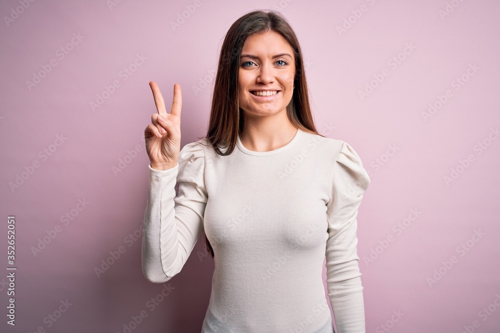 Young beautiful woman with blue eyes wearing casual white t-shirt over pink background showing and pointing up with fingers number two while smiling confident and happy. Young beautiful woman with blue eyes wearing casual white t-shirt over pink background showing and pointing up with fingers number two while smiling confident and happy.