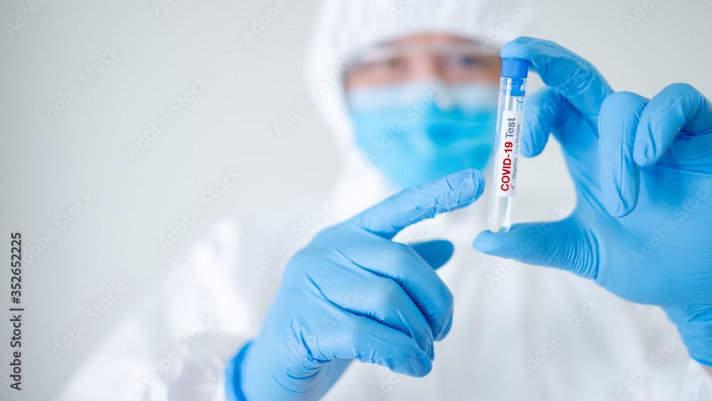 Medical scientist man in personal protective equipment suit (PPE), mask and gloves holding COVID-19 Test tube in hospital laboratory. Male doctor getting result of Coronavirus case. 2019-nCoV research Medical scientist man in personal protective equipment suit (PPE), mask and gloves holding COVID-19 Test tube in hospital laboratory. Male doctor getting result of Coronavirus case. 2019-nCoV research