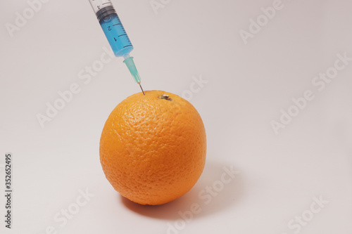 Injecting blue liquid into an orange fruit. Syringes for injection close-up. Genetically modified orange. Injecting liquid from a syringe into an orange. Pesticides used in our food and fruit.