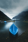 Moody scenery of a boat docked near shore at Klontal Lake. Beautiful moody dark landscape with foggy mountains on the background